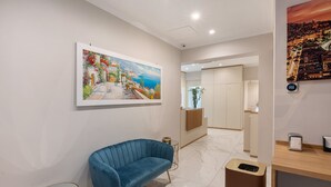 Eine moderne Hotelhalle mit einem blauen Sofa, einem Gemälde einer Küstenlandschaft, einer Rezeption und einem Marmorboden.