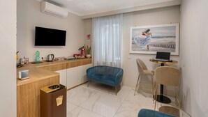 A modern room with a flat-screen TV, a sofa, a small table with a laptop, a window with sheer curtains, and a painting on the wall. - Room 'Luxury  Fronte Mare Con Jacuzzi' with Balcony, Wi-Fi and Air Conditioning (Napoli)