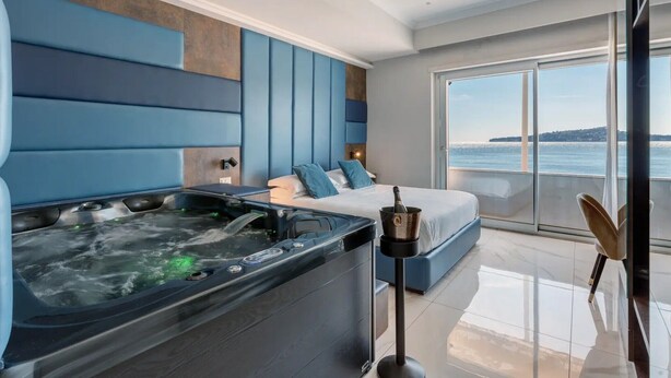 A modern hotel room with a large bed, a hot tub, and a balcony with a view of the sea. - Room Suite with Private Pool, Wi-Fi, and Air Conditioning (Napoli)