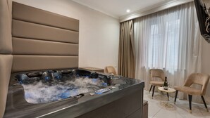 A modern room with a spa tub, two chairs, a small table with a bottle and glass, and a TV mounted on the wall. - Room Suite with Private Pool, Wi-Fi, and Air Conditioning (Napoli)