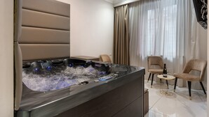 A modern room with a hot tub, two chairs, a small table with a bottle and glass, and a TV mounted on the wall. - Room Suite with Private Pool, Wi-Fi, and Air Conditioning (Napoli)