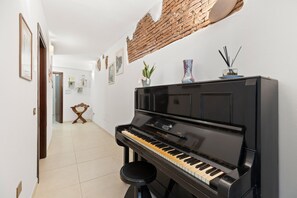 Un couloir avec un piano, un tabouret, un mur en briques et une porte.