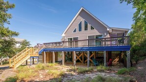 A two-story house with a wooden deck and a staircase leading to the upper level. - Lucky Fin - Corolla, Ocean Sands, Oceanside, 600 Yds to Beach, 4 Bedrooms, Hot Tub, Pets OK! (Corolla)