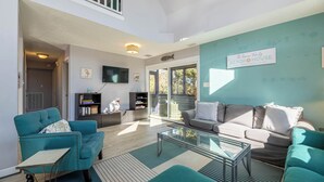 A spacious living area with a large window, a flat-screen TV, and a sign indicating 'The Remani Family Beach House'. - Lucky Fin - Corolla, Ocean Sands, Oceanside, 600 Yds to Beach, 4 Bedrooms, Hot Tub, Pets OK! (Corolla)