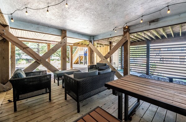 Eine Terrasse im Freien mit Korbmöbeln, einem Holztisch und Lichterketten.