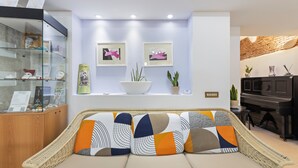 A living room with a sofa, a glass display cabinet, framed artwork, a piano, and a plant. - Room 'Camera 2' with Wi-Fi and Air Conditioning (Oristano)
