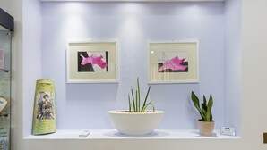 A reception area with a white reception desk, two framed artworks, a potted plant, and a decorative item on the wall. - Room 'Camera 2' with Wi-Fi and Air Conditioning (Oristano)
