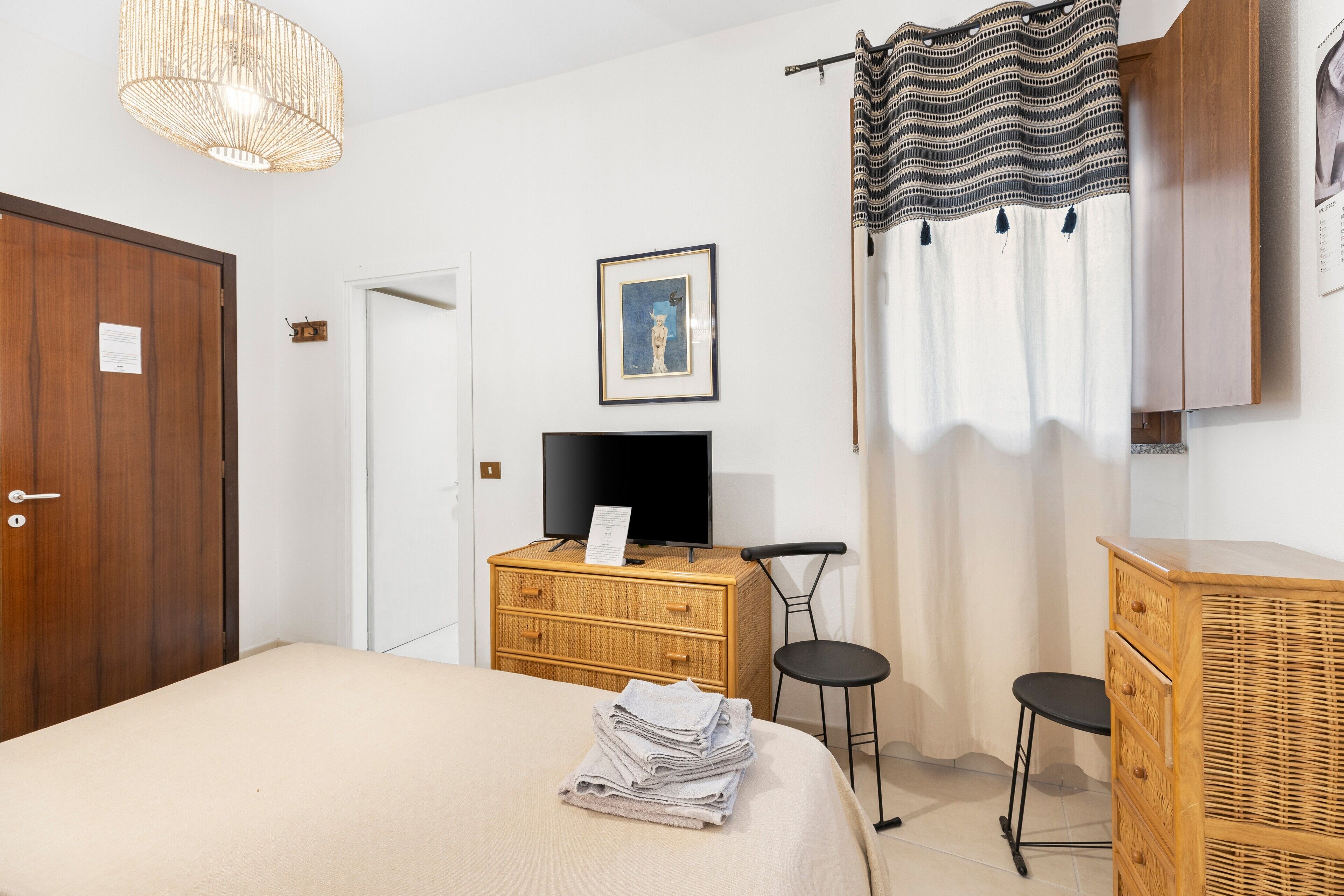 A hotel room with a bed, a television, a wooden dresser, two chairs, and a wall-mounted picture.