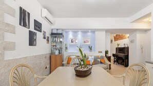 A dining area with a table, chairs, a potted plant, and a piano in the background. - Room 'Camera 2' with Wi-Fi and Air Conditioning (Oristano)