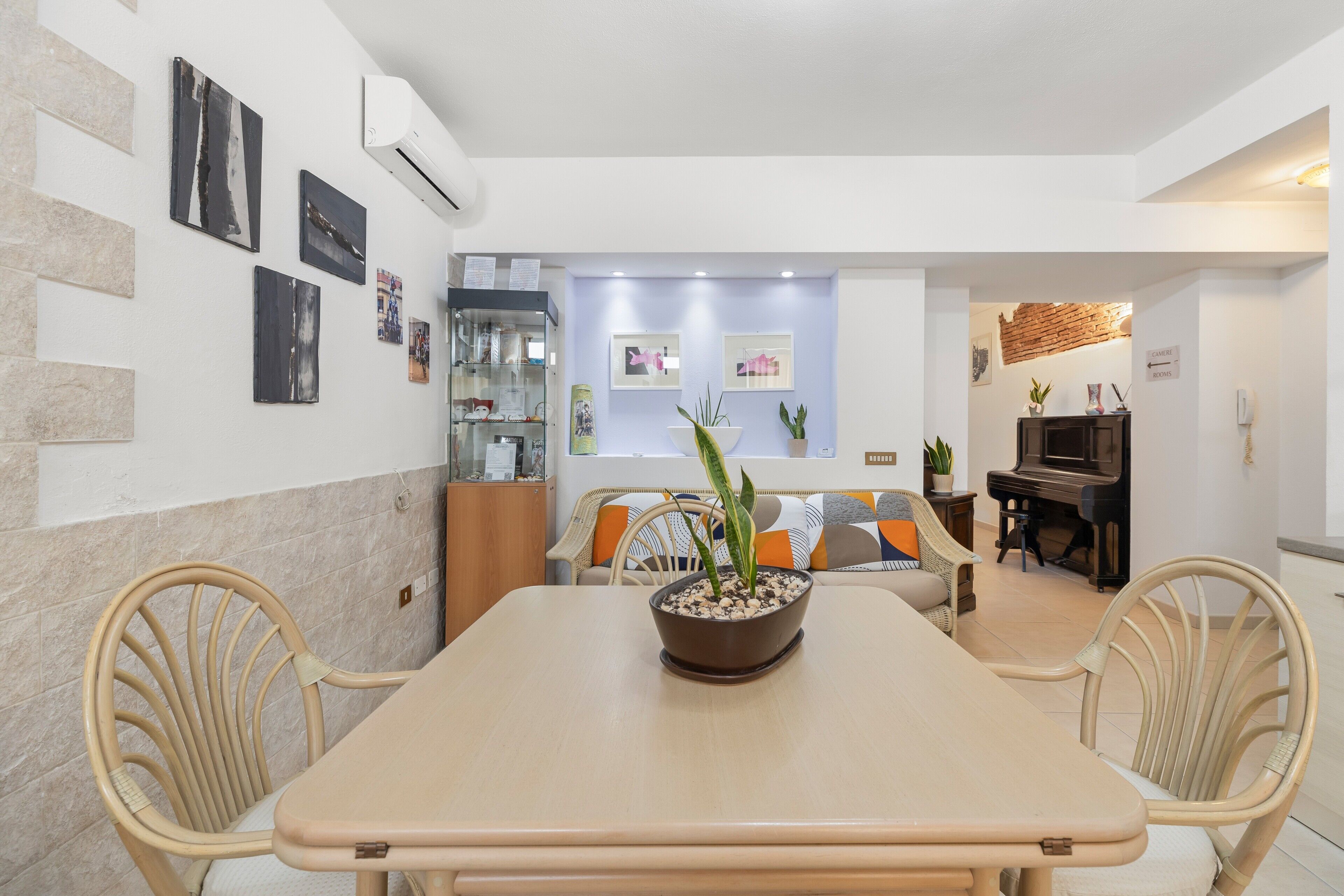 A dining area with a table, chairs, a potted plant, and a piano in the background.