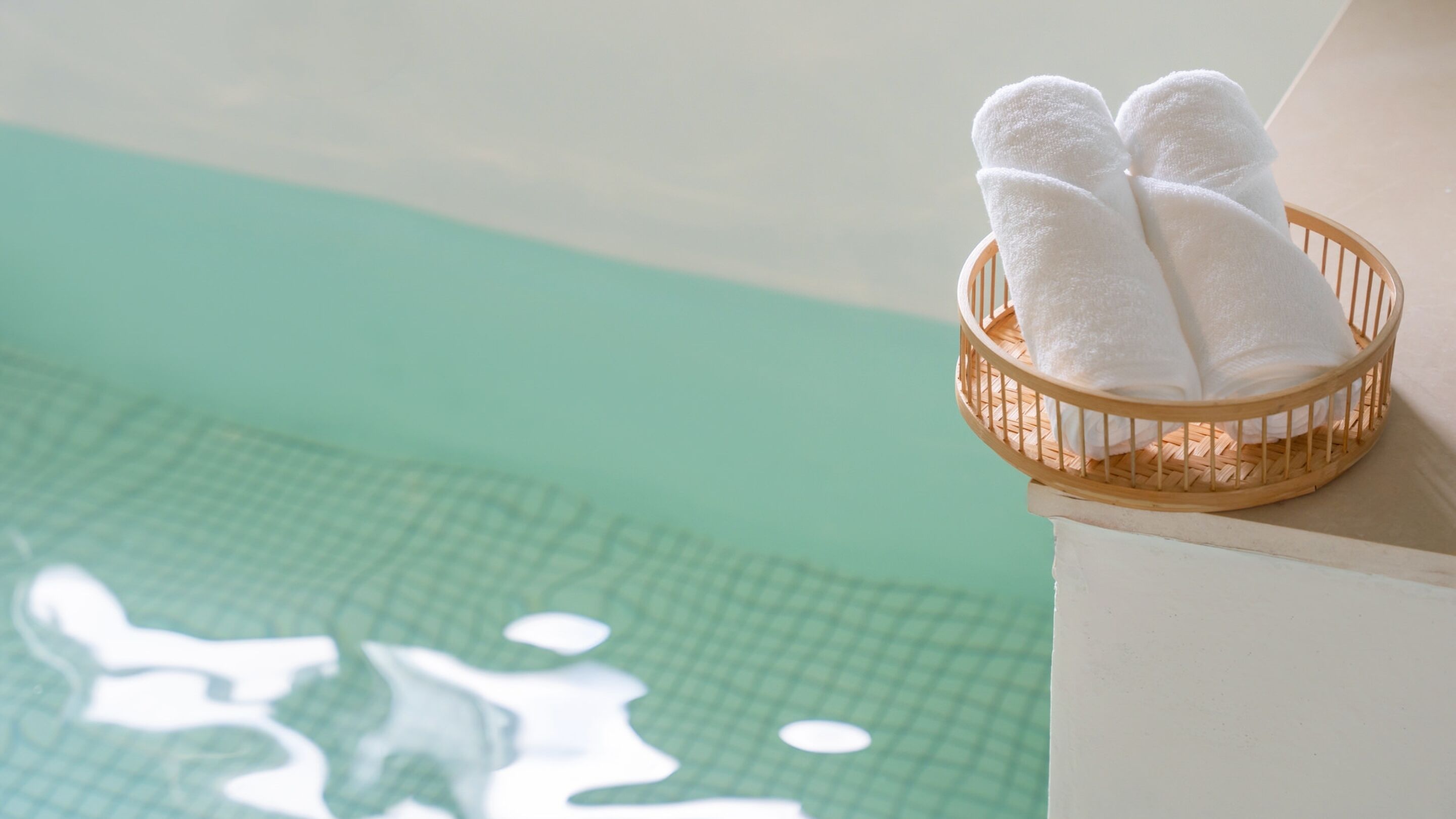 A wooden basket with white towels on a poolside.