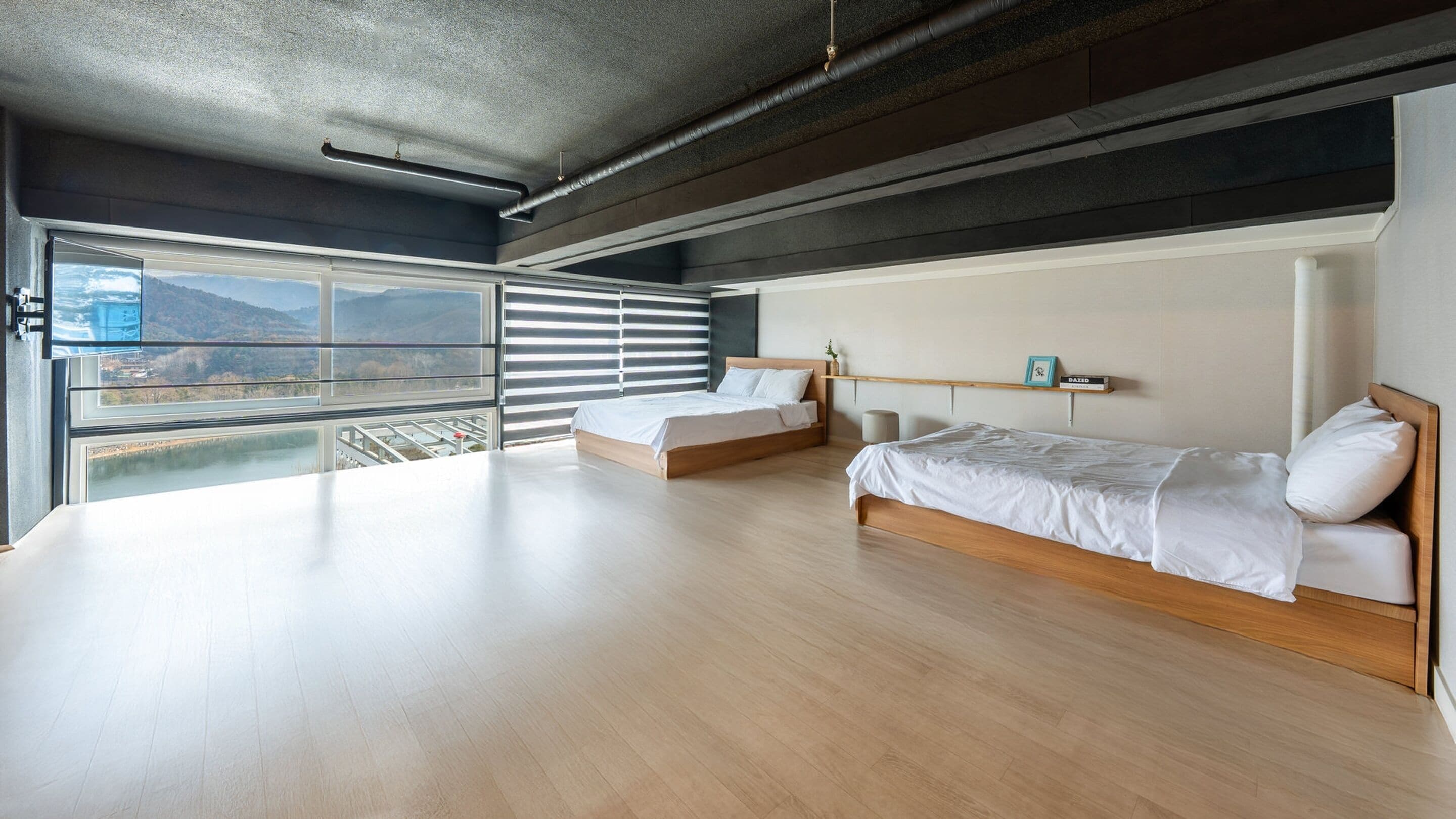 Une chambre moderne avec deux lits, de grandes fenêtres et une vue sur l’extérieur.