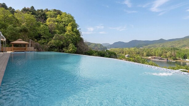 Une piscine dotée d’une terrasse en bois et d’un kiosque, entourée d’une végétation luxuriante et offrant une vue sur la rivière.