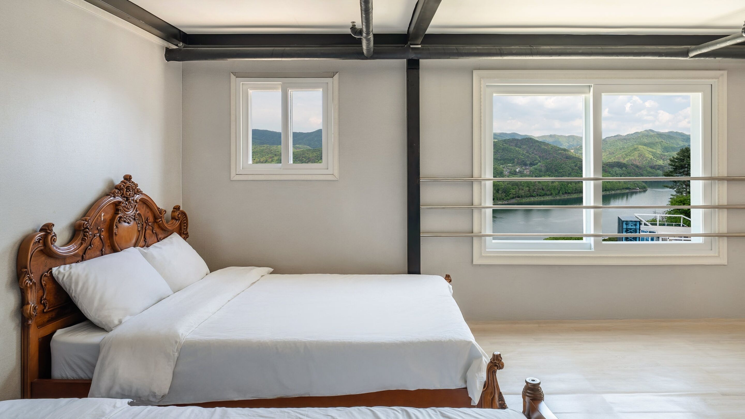 Un dormitorio con una cama grande, una cama más pequeña y una ventana con vistas a un lago y montañas.