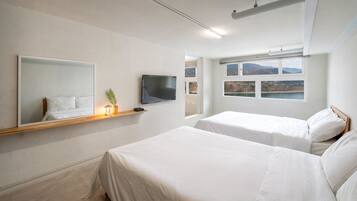 A hotel room with two beds, a TV, a shelf with a plant, and a window with a mountain view.