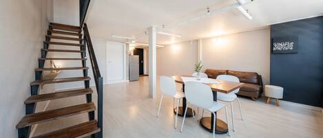 A modern interior with a wooden staircase, a dining area with a table and chairs, a leather sofa, and a dark accent wall.