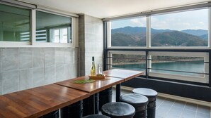 Une cuisine moderne avec un plan de travail en bois, des tabourets noirs et une vue sur les montagnes et un lac, grâce à de grandes fenêtres.