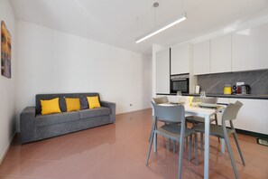 A modern kitchen with white cabinets, a grey sofa with yellow cushions, and a dining table with chairs.
