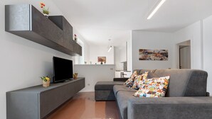 Een moderne woonkamer met een grijze bank, een flatscreen televisie en een minimalistisch design.