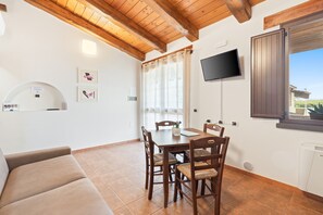 Un coin repas avec une table et des chaises en bois, un téléviseur fixé au mur et une fenêtre avec des rideaux.