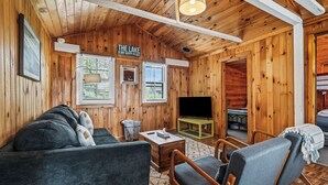 A cozy cabin interior with a sofa, chairs, a television, and a fireplace. - RC 17 – Cozy Cabin with Shared Rangeley Lake Waterfront, Kayaks, Paddleboards & Firepit (Rangeley)