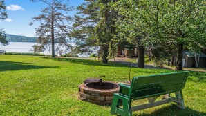A grassy area with a green bench and a stone well. - RC 17 – Cozy Cabin with Shared Rangeley Lake Waterfront, Kayaks, Paddleboards & Firepit (Rangeley)