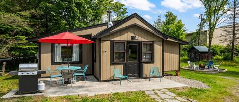 A small cabin with a patio, outdoor seating, and a grill.