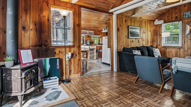 A wooden interior with a sofa, a fireplace, a dining area, and a kitchen. - RC 17 – Cozy Cabin with Shared Rangeley Lake Waterfront, Kayaks, Paddleboards & Firepit (Rangeley)