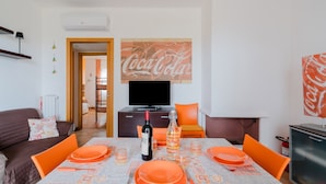 Un coin repas avec une table dressée pour quatre personnes, une bouteille de vin et un téléviseur en arrière-plan.