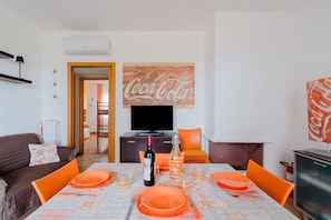 A dining area with a table set for four, a bottle of wine, and a television in the background.