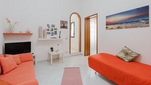 A room with a bed, a sofa, a TV, a painting, and a mirror.