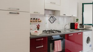 A modern kitchen with white cabinets, a gas stove, a microwave, and a washing machine.