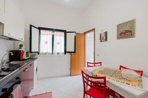 Une cuisine compacte équipée d’un four à micro-ondes, d’une cuisinière et d’un évier. On aperçoit une table à manger avec des chaises rouges et un chemin de table à motifs.