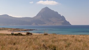 Een kustlandschap met een opvallende berg, een strand en een heldere lucht.