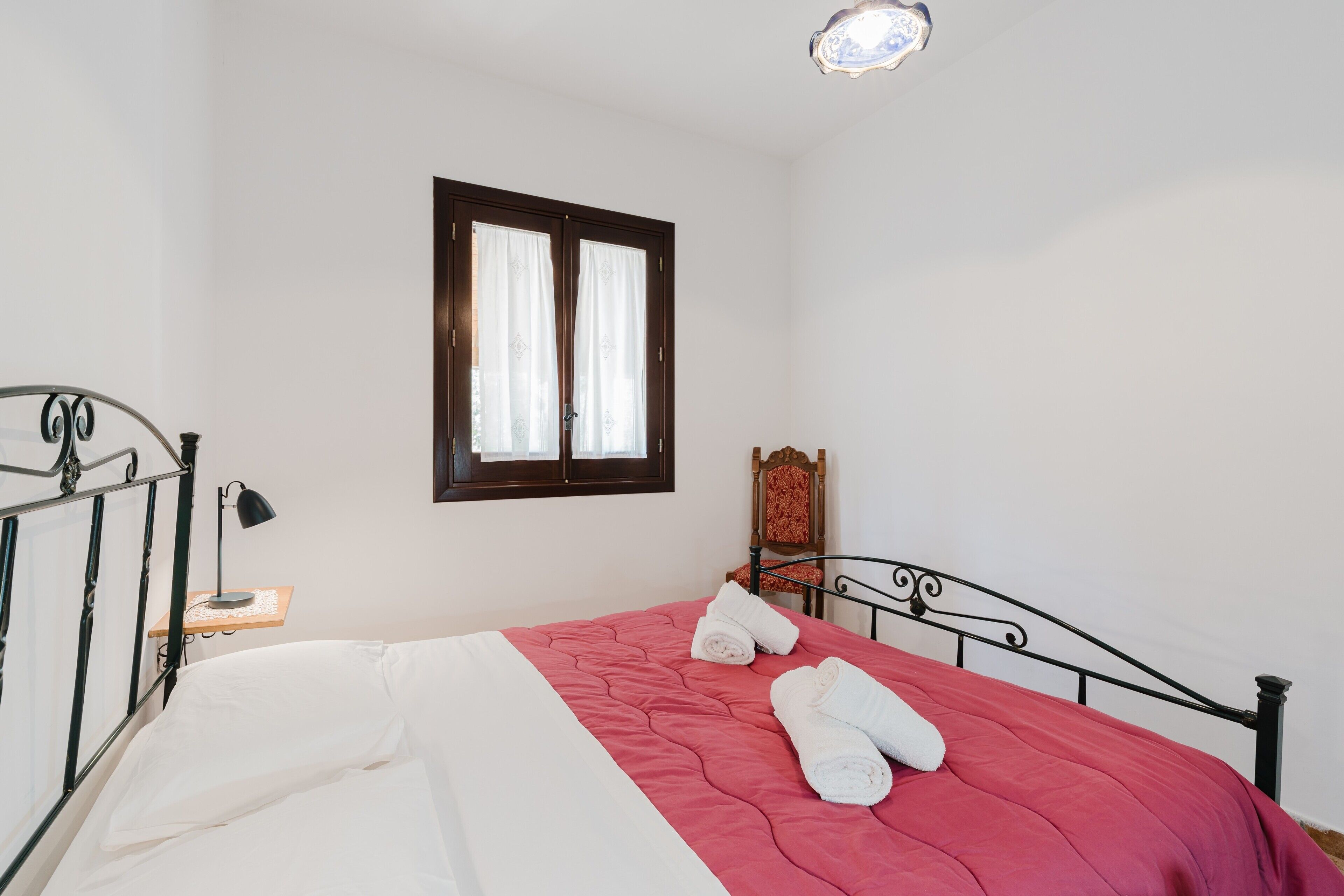 Ein Einzelbett mit roter Bettdecke, weißer Bettwäsche und zwei zusammengerollten Handtüchern.