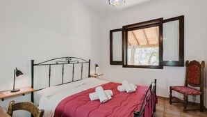 Een slaapkamer met een bed, een stoel, een bureau, een lamp en een raam met uitzicht.