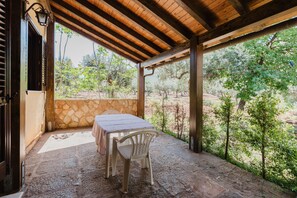 A covered patio with a table and chairs, stone walls, and a view of trees and landscape.