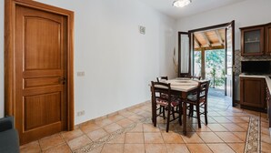 Een eetruimte met een houten tafel en stoelen, een keuken met kasten, en een deur die naar buiten leidt.