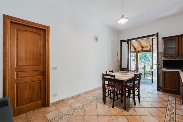 A dining area with a wooden table and chairs, a kitchen with cabinets, and a door leading outside.