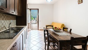 A kitchen with a sink, wooden cabinets, a dining table with chairs, and a view through an open door. - Apartment 'Tra Mare E Natura, Solo Relax' with Mountain View, Wi-Fi and Air Conditioning (Castelluzzo)