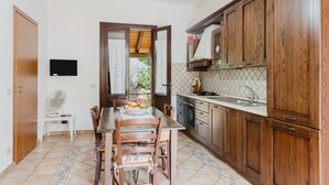 A kitchen with wooden cabinets, a dining table with chairs, a fan, and a view of greenery outside. - Apartment 'Tra Mare E Natura, Solo Relax' with Mountain View, Wi-Fi and Air Conditioning (Castelluzzo)
