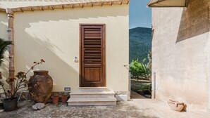A building with a wooden door, steps leading to the entrance, and potted plants outside. - Apartment 'Tra Mare E Natura, Solo Relax' with Mountain View, Wi-Fi and Air Conditioning (Castelluzzo)