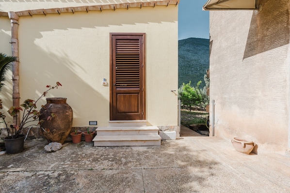A building with a wooden door, steps leading to the entrance, and potted plants outside.