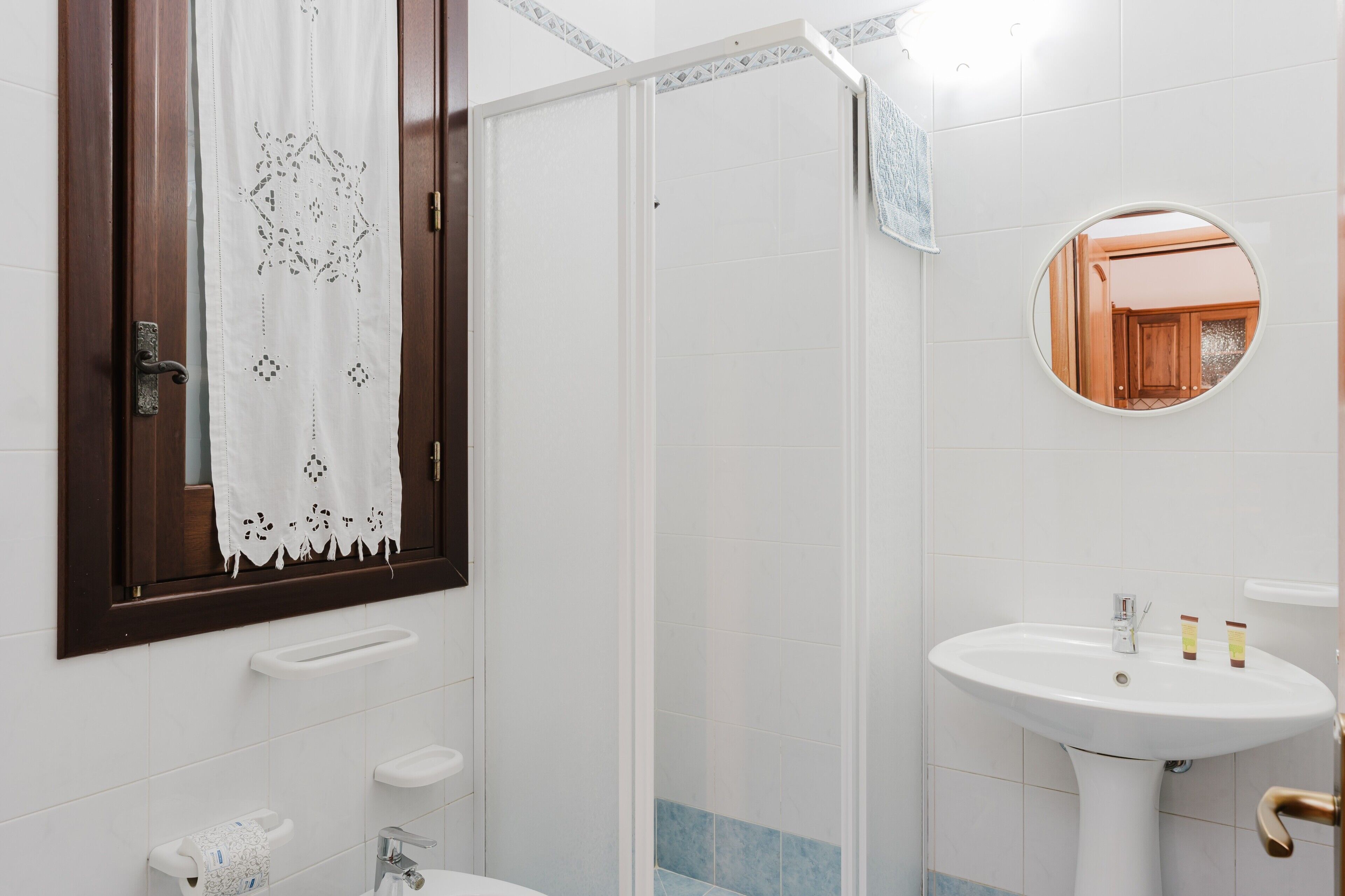 Ein Badezimmer mit weißem Waschbecken, einer Glasdusche, einer Holztür und einem Spiegel.
