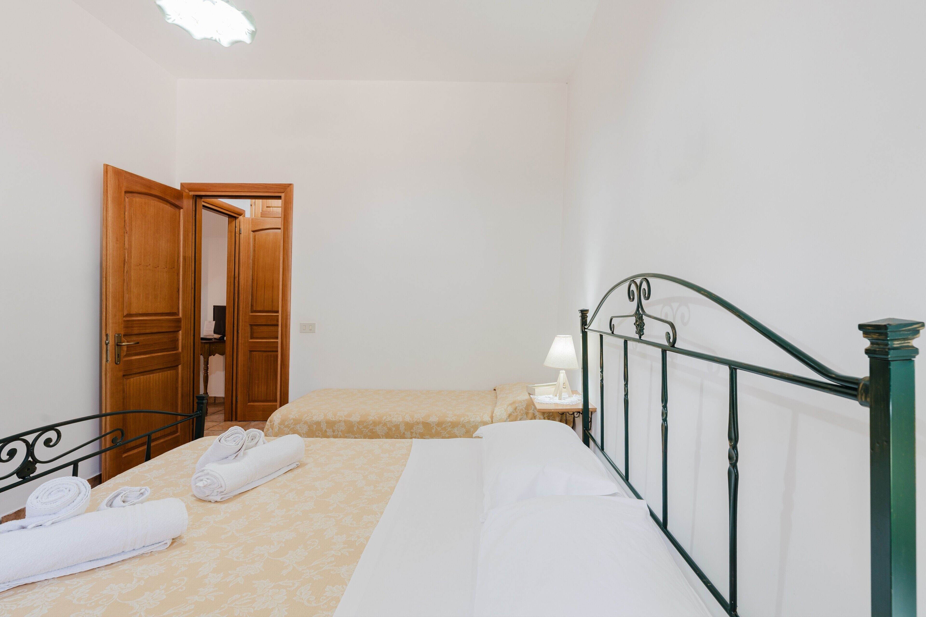 A bedroom with two beds, a wooden door, a nightstand with a lamp, and a metal railing.