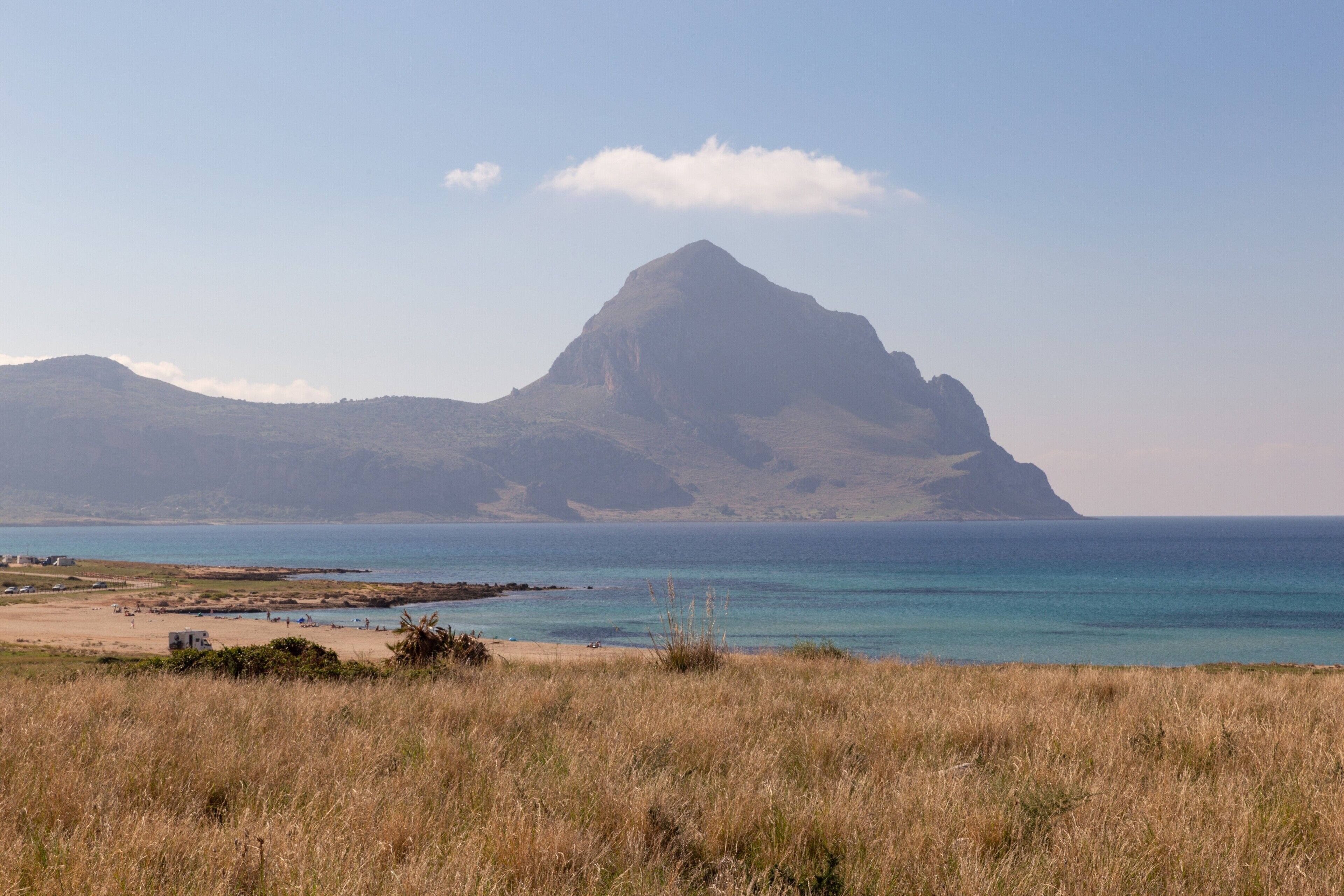 Ett kustlandskap med ett framträdande berg, en strand och en klar himmel.