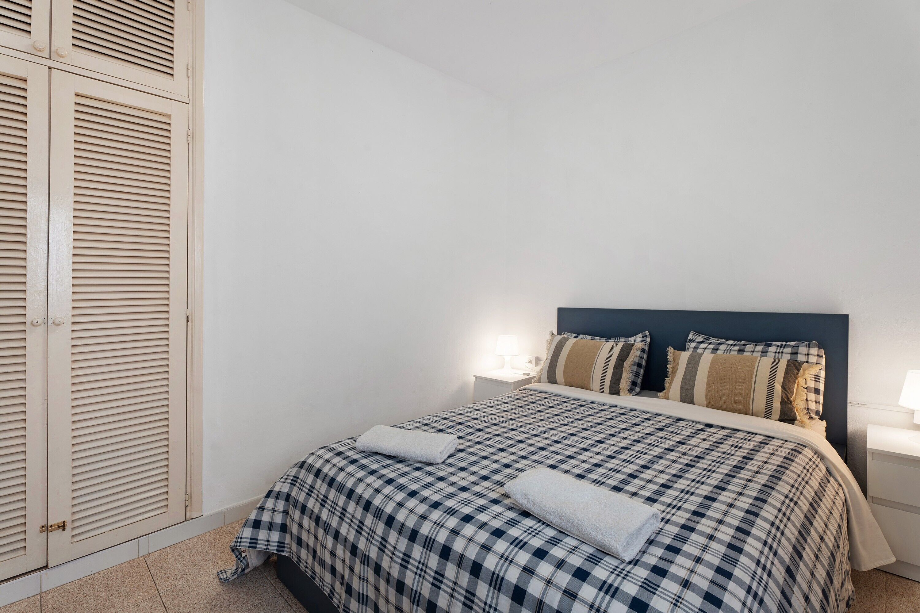 A bedroom with a bed, pillows, a nightstand, and a wardrobe.