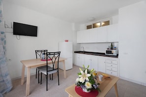A modern kitchen with white cabinets, a microwave, and a flat-screen TV mounted on the wall.