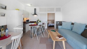 Een ruimtelijke leefruimte met kitchenette, eethoek en een bank.