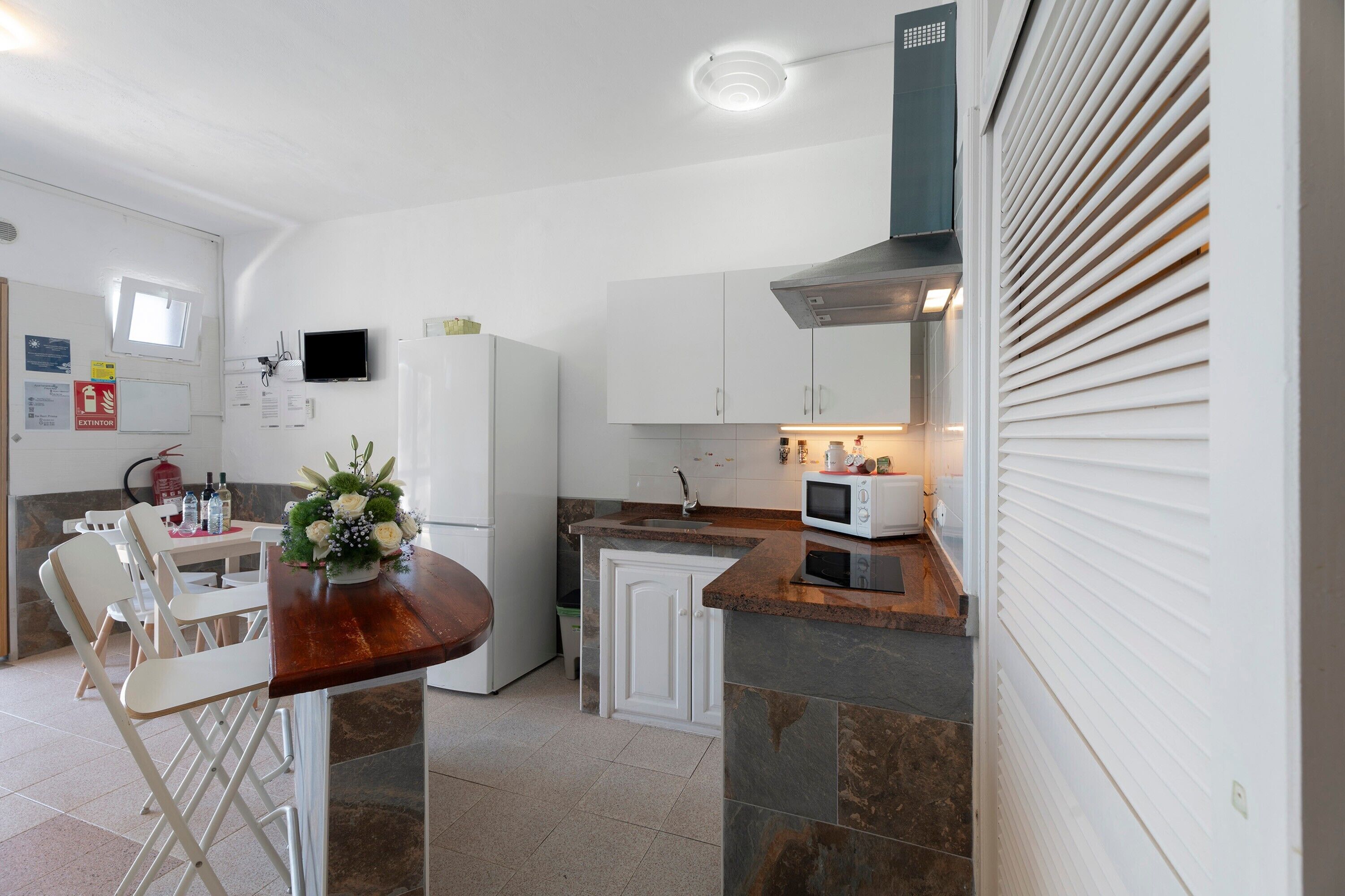 A compact kitchen with white cabinets, a microwave, and a sink. There is a dining area with chairs and a table.